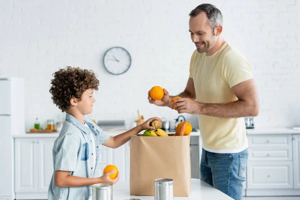 Sorridente padre e figlio che prendono cibo dal sacchetto di carta in cucina — Foto stock