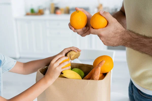 Vista recortada de padre e hijo sosteniendo frutas cerca de la bolsa de papel en casa - foto de stock