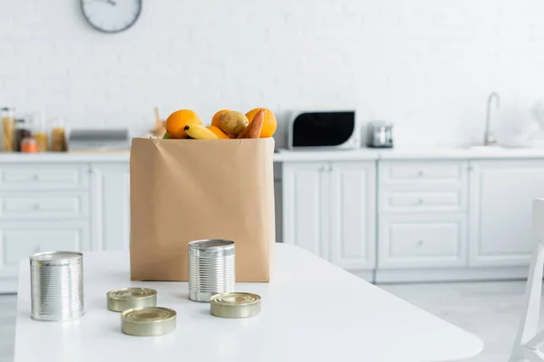 Latas de lata y comida en bolsa de papel en cocina - foto de stock