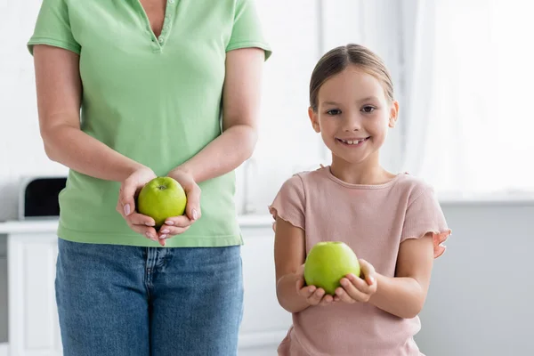 Lächelndes Kind hält Apfel neben Mutter in Küche — Stockfoto