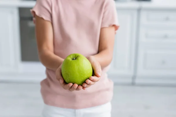 Cropped view of green apple in hands of blurred kid — Stock Photo