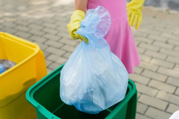 Vue recadrée de fille tenant sac poubelle près de la poubelle à l'extérieur — Photo de stock