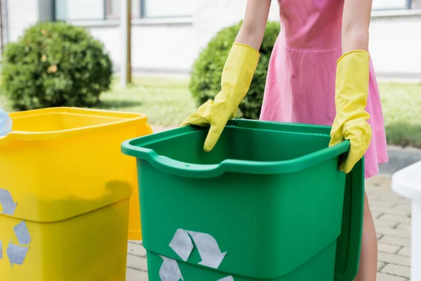 Ausgeschnittene Ansicht eines Kindes in Gummihandschuhen, das in der Nähe von Mülltonnen mit Recyclingschild im Freien steht — Stockfoto