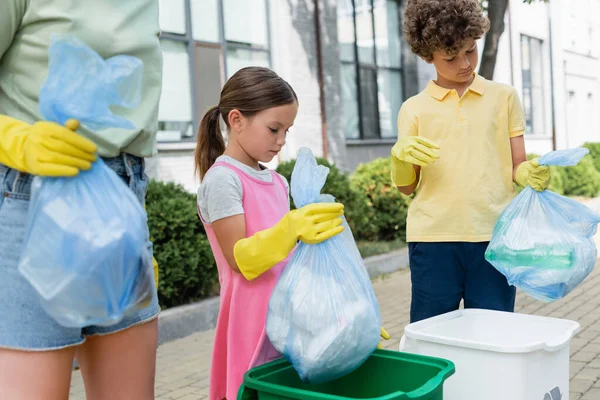 Enfants tenant des sacs poubelles près des canettes et mère floue à l'extérieur — Photo de stock