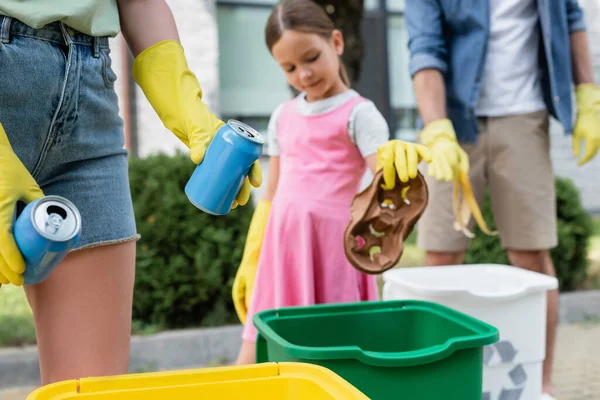 Frau hält Blechdosen neben verschwommener Familie und Mülltonnen im Freien — Stockfoto