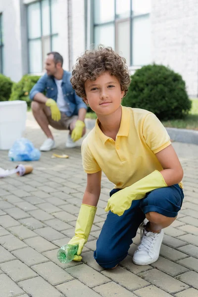 Niño en guantes de goma tomando basura de la tierra al aire libre - foto de stock