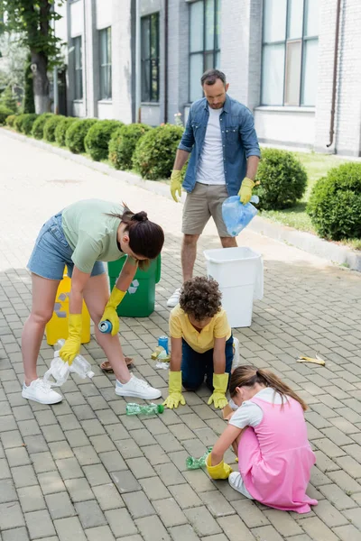 Familia en guantes de goma clasificando la basura cerca de latas en la calle urbana - foto de stock