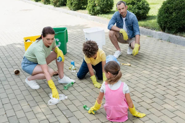 Familie mit Kindern in Gummihandschuhen sammelt Müll in der Nähe von Mülltonnen im Freien — Stockfoto