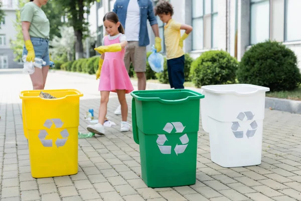 Trash cans with recycle sign near blurred family outdoors — Stock Photo