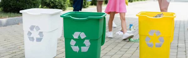 Cropped view of trash cans with recycle symbol near blurred family outdoors, banner — Stock Photo