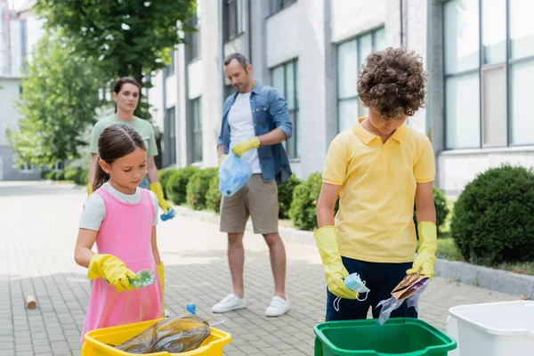 Enfants tenant des ordures près des canettes et parents flous dans la rue urbaine — Photo de stock