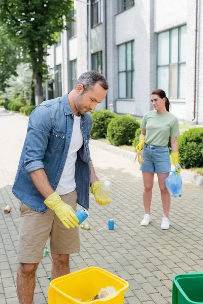 Homme adulte en gants de caoutchouc triant les ordures près des canettes à l'extérieur — Photo de stock