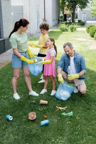 Positive parents with kids collecting trash on lawn — Stock Photo