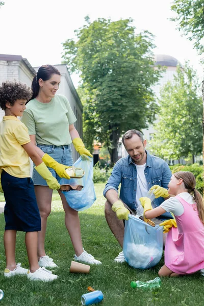 Happy children and parents in rubber gloves collecting trash on grass — Stock Photo