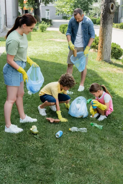 Famille en gants de caoutchouc ramassant les ordures sur l'herbe à l'extérieur — Photo de stock