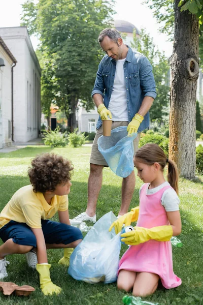 Чоловік кладе сміття в сумку біля дітей на газоні — стокове фото