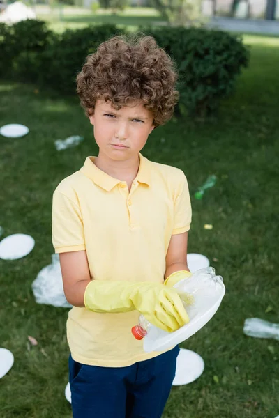 Хлопчик в гумових рукавичках тримає сміття і дивиться на камеру на відкритому повітрі — стокове фото