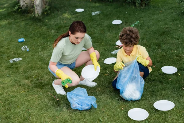 Aus der Vogelperspektive: Mutter und Sohn sammeln Müll in der Nähe von Säcken auf dem Rasen auf — Stockfoto