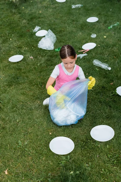High angle view of girl in rubber gloves collecting trash in bag on lawn — Stock Photo