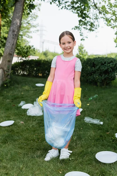 Happy kid holing trash bag near garbage on grass — Stock Photo