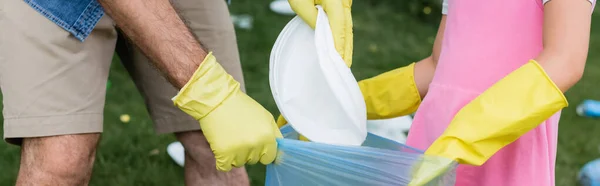 Cropped view of man and girl in rubber gloves putting trash in bag outdoors, banner — Stock Photo