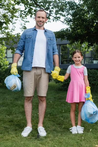 Padre sorridente che si tiene per mano figlia e sacco della spazzatura sul prato — Foto stock