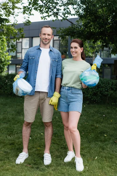 Adult couple holding trash bags and smiling at camera outdoors — Stock Photo
