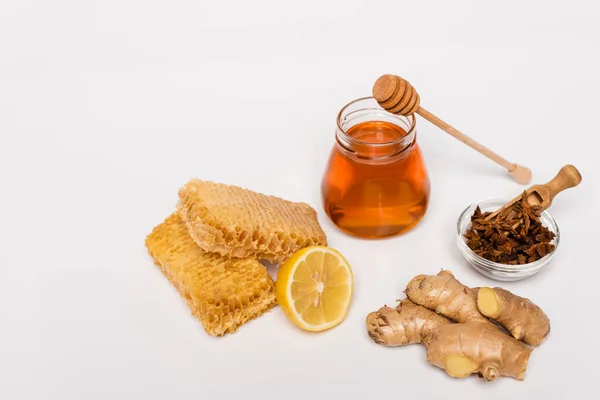 Pot de miel près de trempette en bois, bol avec graines d'anis, nid d'abeille, citron frais et racine de gingembre sur blanc — Photo de stock