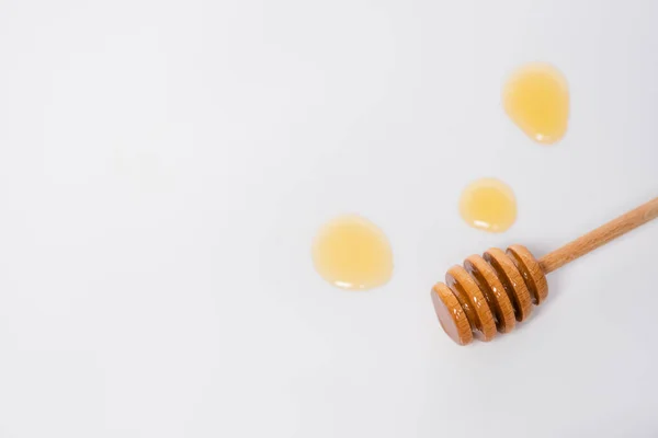 Vista superior del cazo de madera cerca de gotas de miel sobre fondo blanco con espacio para copiar — Stock Photo