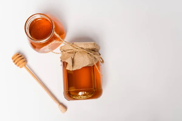 Top view of honey stick near jars with honey on white surface — Stock Photo