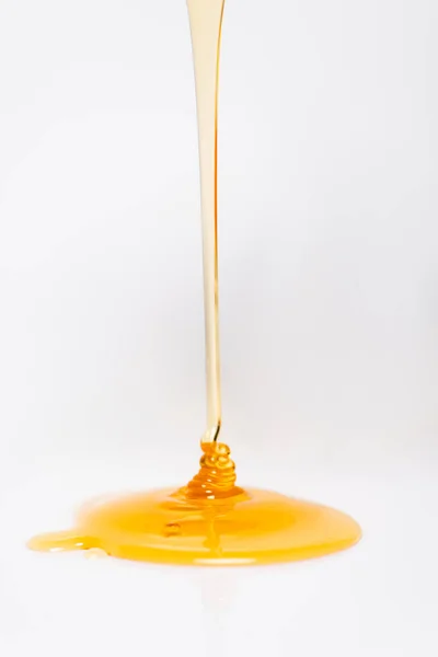 Trickle of fresh golden honey flowing on white — Stock Photo