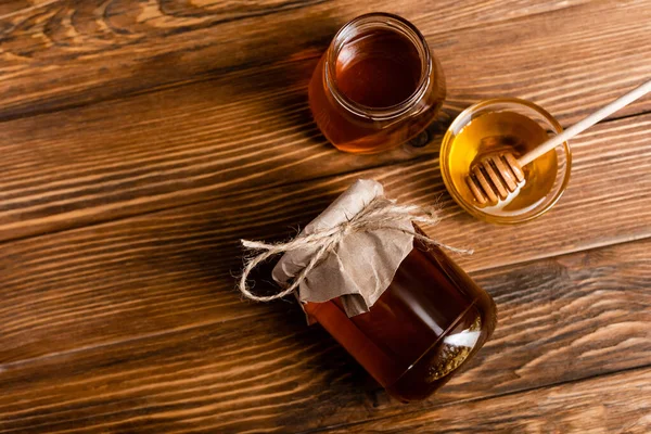 Vista superior de frascos de mel e tigela com dipper na superfície de madeira marrom — Fotografia de Stock