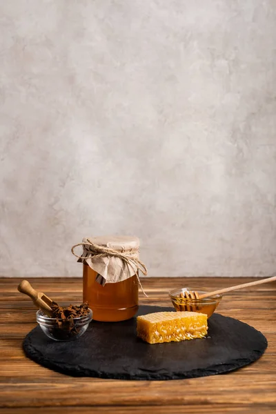 Jar and bowls with honey, anise seeds, honeycomb and slate board on grey marble background — Stock Photo