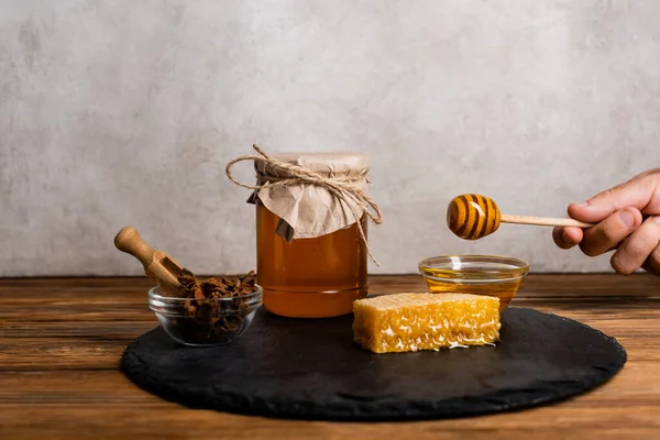 Частичный вид человека с деревянной ковшой рядом с чашей с семенами аниса и банкой с медом на сером мраморном фоне — стоковое фото