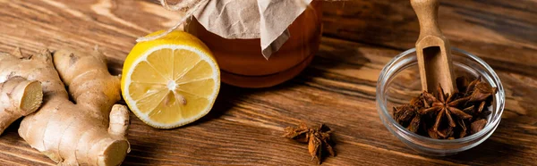 Honey jar, juicy lemon, ginger root and jar with anise seeds and scoop on wooden table, banner — Stock Photo