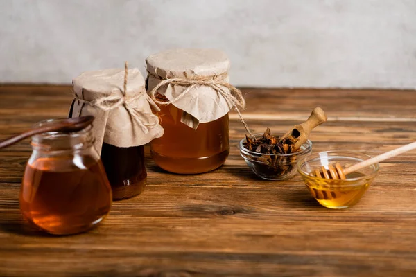 Gläser und Schalen mit Honig und Aniskernen auf Holztisch und grauem Hintergrund — Stockfoto