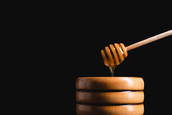 Liquid honey flowing from dipper into small wooden barrel isolated on black — Stock Photo