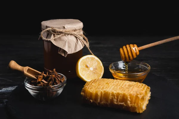 Ciotole con miele e semi di anice vicino a nido d'ape, limone fresco e vaso isolato su nero — Foto stock