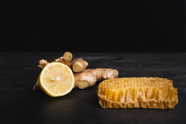 Citron juteux près de la racine de gingembre et nid d'abeille sur une surface sombre isolé sur noir — Photo de stock