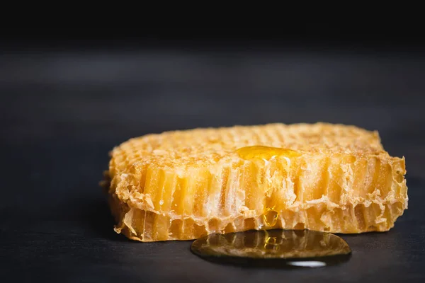 Vista de perto de favo de mel com mel dourado na superfície escura isolada em preto — Fotografia de Stock