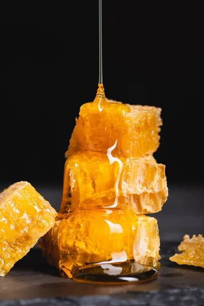 Close up view of liquid honey dripping on cut honeycomb isolated on black — Stock Photo