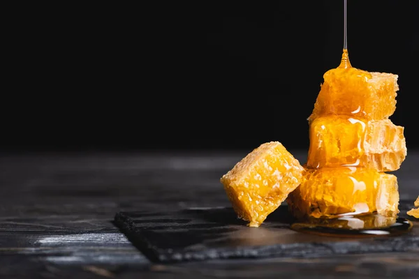 Mel dourado que flui em pedaços de favo de mel na superfície escura isolada em preto — Fotografia de Stock