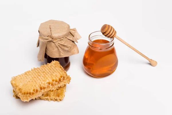 Jars with yellow and brown honey near wooden dipper and honeycomb on white — Stock Photo