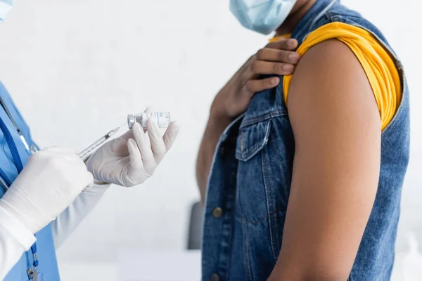 Cropped view of nurse in latex gloves holding vaccine near african american man in medical mask — Stock Photo
