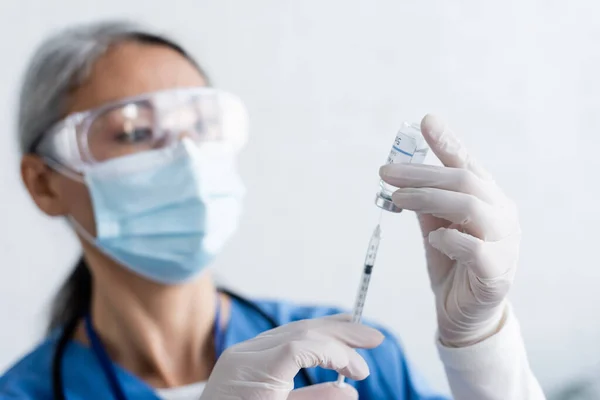 Immunologo asiatico offuscata in maschera medica e occhiali tenendo siringa e vaso con vaccino — Foto stock