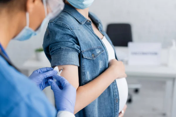 Vue recadrée de l'infirmière floue vaccinant la femme enceinte à la clinique — Photo de stock