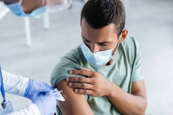 Infirmière floue injectant le vaccin au jeune homme sous masque protecteur — Photo de stock