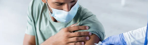 Врач вакцинирует молодого человека в медицинской маске, баннер — стоковое фото