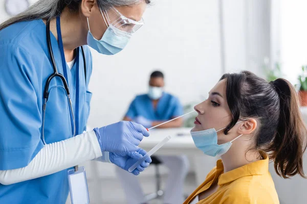Maduro asiático médico em médico máscara tomando amostras para pcr teste de jovem mulher no hospital — Fotografia de Stock