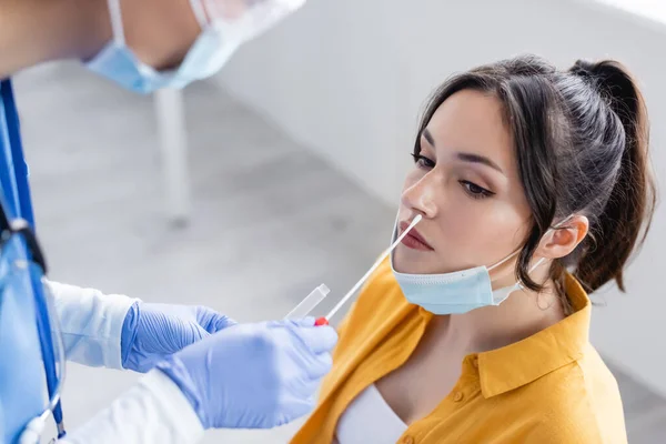 Médico desfocado em máscara médica e luvas de látex fazendo teste de swab nasal de mulher na clínica — Stock Photo